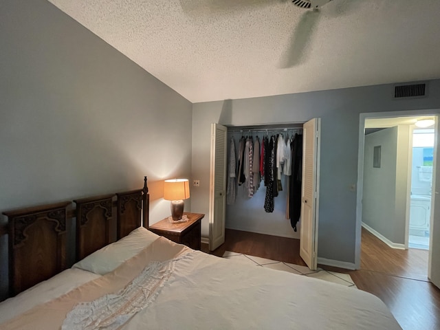 bedroom with a textured ceiling, light wood-type flooring, a closet, and ensuite bath