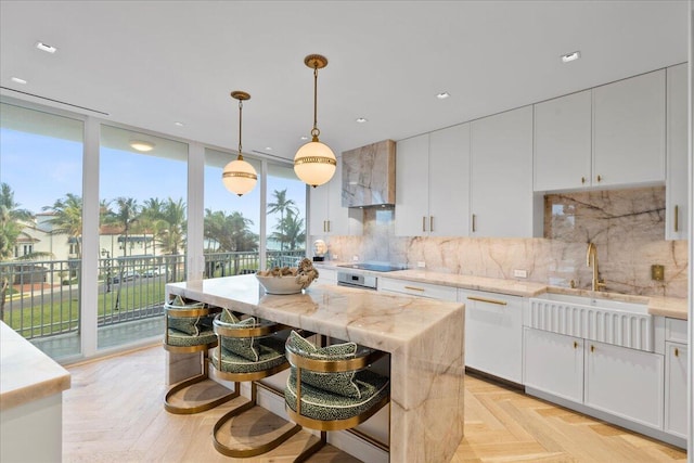 kitchen with white cabinetry, wall chimney exhaust hood, tasteful backsplash, a kitchen island, and a wall of windows