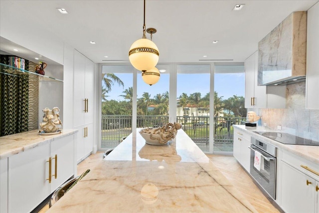 kitchen with light stone counters, hanging light fixtures, white cabinets, and oven