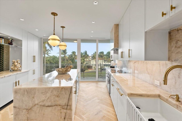 kitchen with floor to ceiling windows, light stone countertops, white cabinetry, sink, and hanging light fixtures