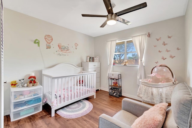 bedroom featuring ceiling fan, wood-type flooring, and a nursery area