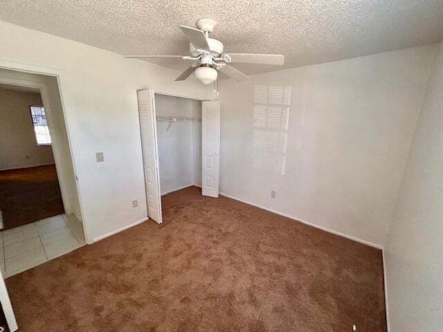 unfurnished bedroom with dark colored carpet, a textured ceiling, a closet, and ceiling fan