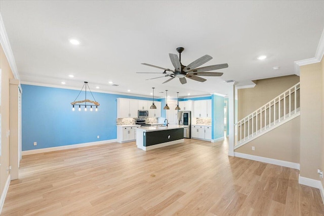 kitchen featuring stainless steel appliances, decorative light fixtures, a center island with sink, light hardwood / wood-style flooring, and white cabinets