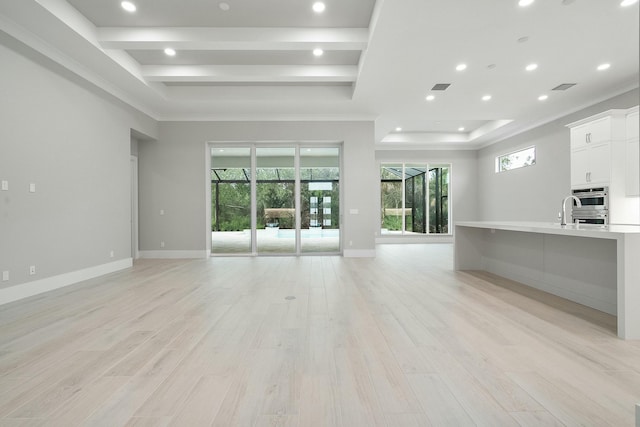 unfurnished living room featuring a raised ceiling, sink, ornamental molding, and light wood-type flooring