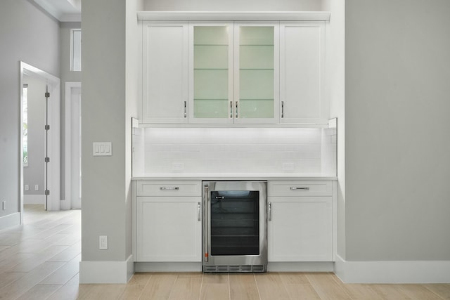 bar with tasteful backsplash, white cabinets, and beverage cooler