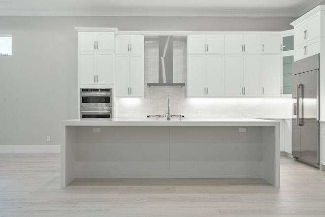 kitchen with white cabinets, wall chimney range hood, an island with sink, and appliances with stainless steel finishes