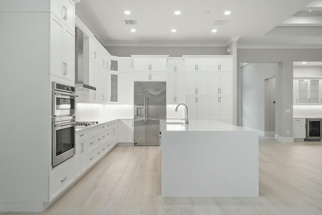 kitchen with stainless steel appliances, white cabinetry, beverage cooler, and a center island with sink