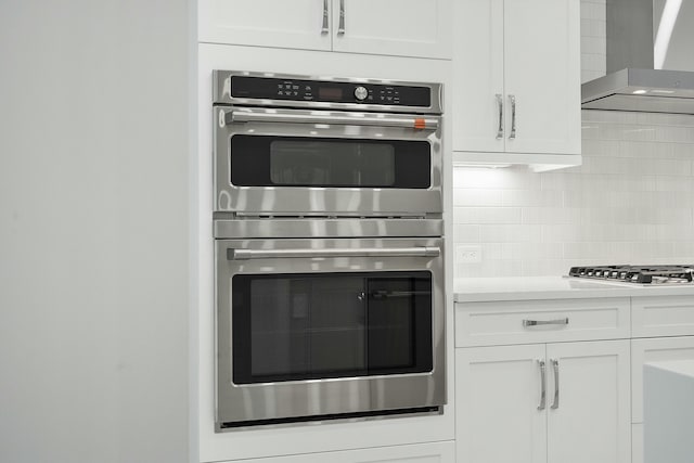 kitchen featuring stainless steel appliances, white cabinetry, tasteful backsplash, and wall chimney exhaust hood