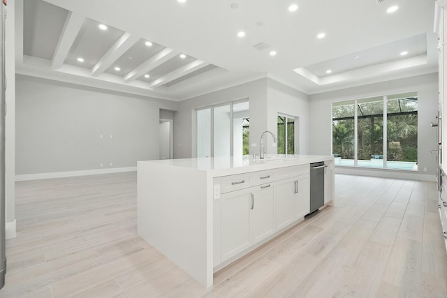 kitchen featuring white cabinetry, sink, a raised ceiling, light hardwood / wood-style flooring, and a center island with sink