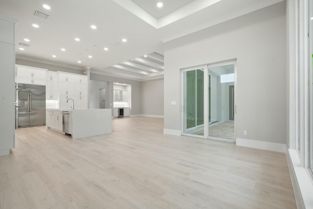 unfurnished living room featuring beamed ceiling, light hardwood / wood-style floors, ornamental molding, and sink