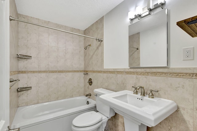 full bathroom with tile walls, shower / bathing tub combination, toilet, a sink, and a textured ceiling