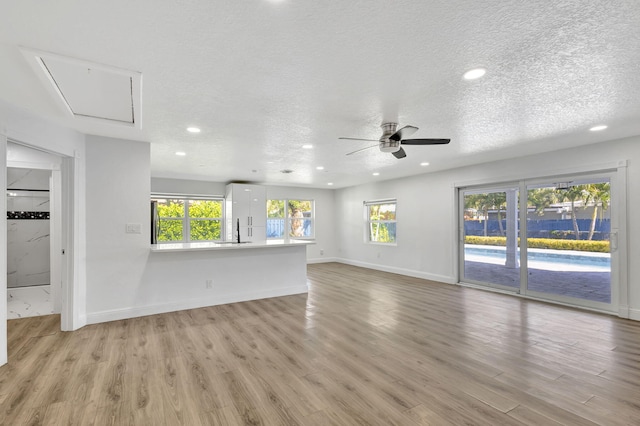 unfurnished living room featuring ceiling fan, sink, a textured ceiling, and light hardwood / wood-style flooring