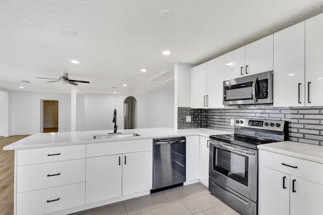 kitchen featuring kitchen peninsula, stainless steel appliances, ceiling fan, sink, and white cabinets