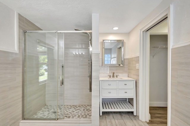 full bath with a stall shower, wood finished floors, a walk in closet, vanity, and tile walls