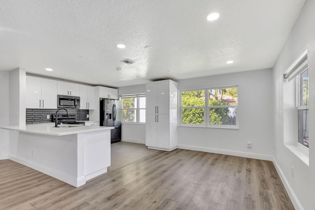 kitchen featuring white cabinets, a peninsula, stainless steel appliances, and light countertops