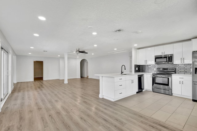 kitchen with light countertops, appliances with stainless steel finishes, open floor plan, white cabinetry, and a peninsula