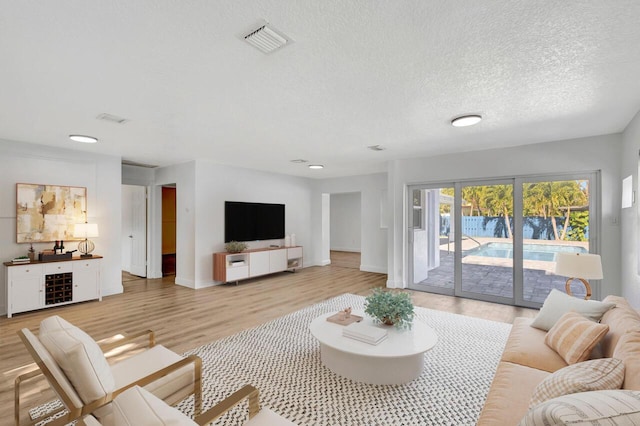 living room with light wood finished floors, baseboards, visible vents, and a textured ceiling