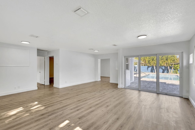 spare room with a textured ceiling, light wood-style flooring, visible vents, and baseboards