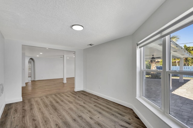 empty room with baseboards, visible vents, arched walkways, wood finished floors, and a textured ceiling