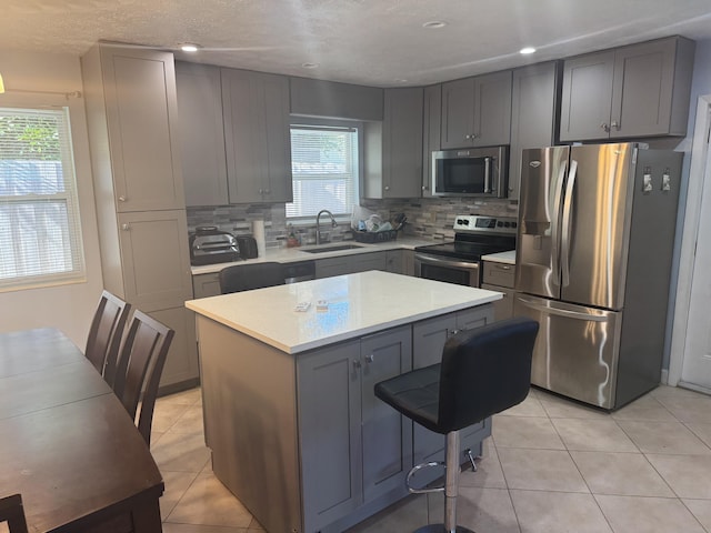 kitchen with sink, a center island, appliances with stainless steel finishes, gray cabinets, and backsplash