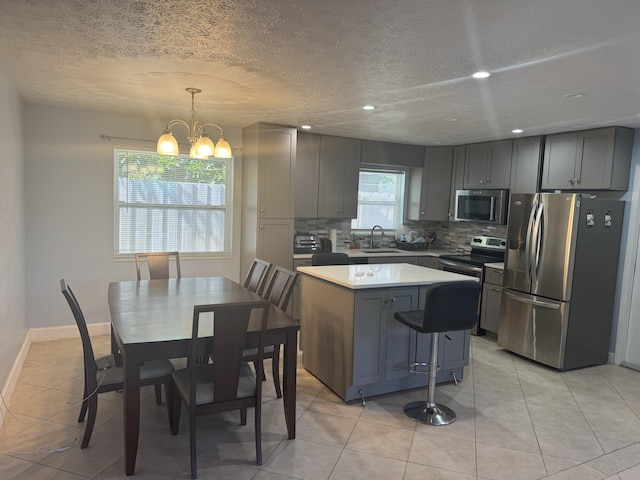 kitchen with sink, hanging light fixtures, stainless steel appliances, decorative backsplash, and a kitchen island