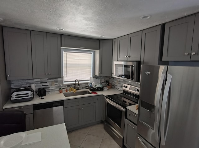 kitchen with gray cabinets, sink, backsplash, light tile patterned floors, and stainless steel appliances