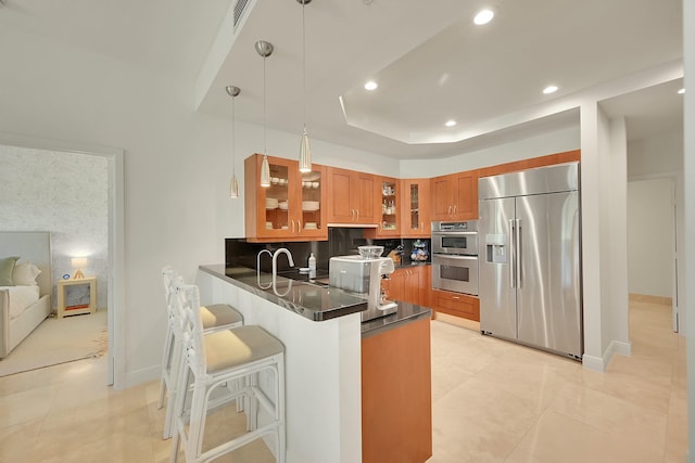 kitchen featuring backsplash, a raised ceiling, hanging light fixtures, appliances with stainless steel finishes, and kitchen peninsula