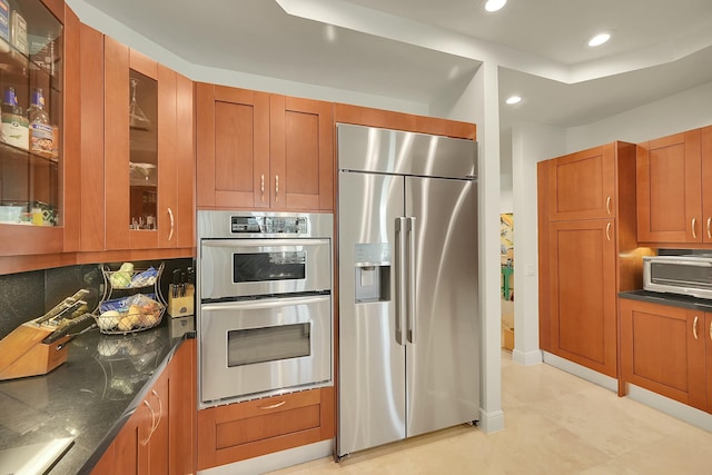 kitchen with backsplash, stainless steel appliances, a raised ceiling, and dark stone countertops