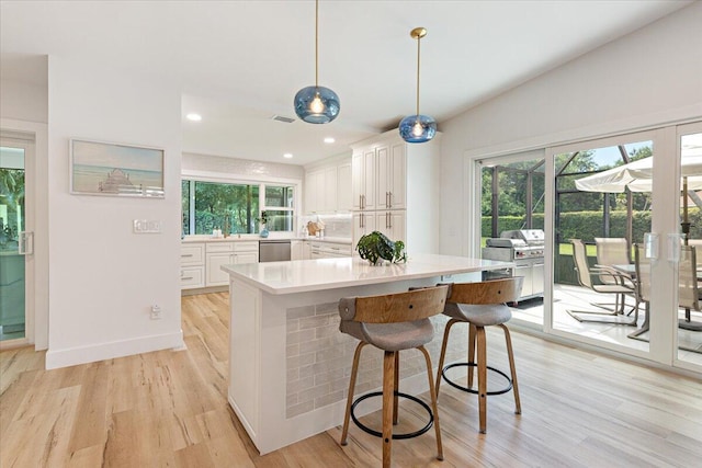 kitchen featuring stainless steel dishwasher, light hardwood / wood-style flooring, white cabinetry, hanging light fixtures, and a breakfast bar area