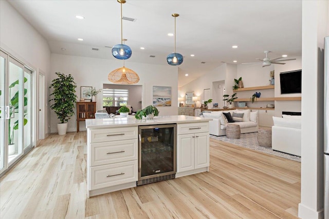 kitchen with beverage cooler, ceiling fan, pendant lighting, white cabinets, and light hardwood / wood-style floors