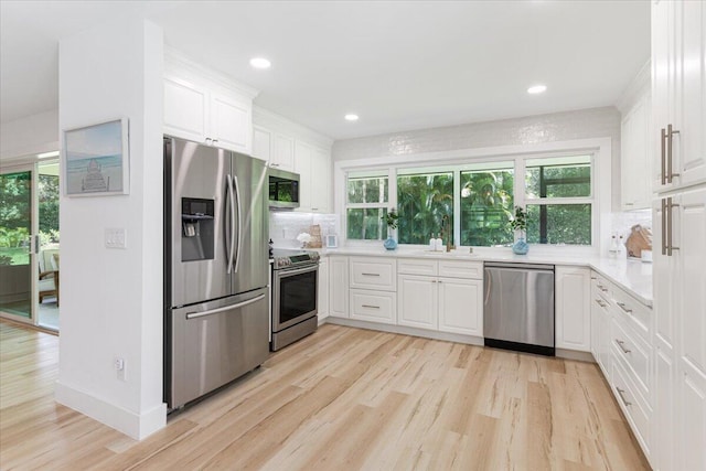 kitchen featuring white cabinets, appliances with stainless steel finishes, light wood-type flooring, and tasteful backsplash