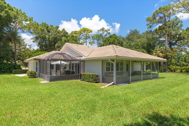 rear view of property featuring a lawn and glass enclosure