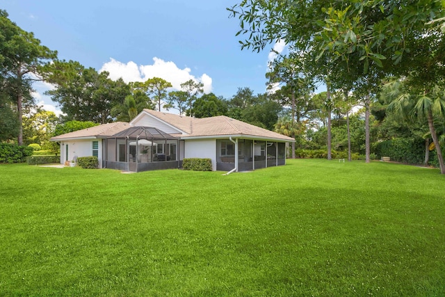 rear view of property with glass enclosure and a yard