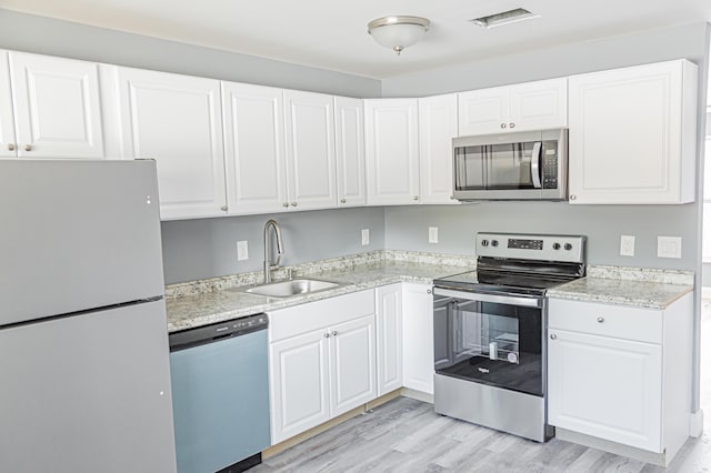 kitchen with white cabinets, sink, light stone countertops, appliances with stainless steel finishes, and light hardwood / wood-style floors