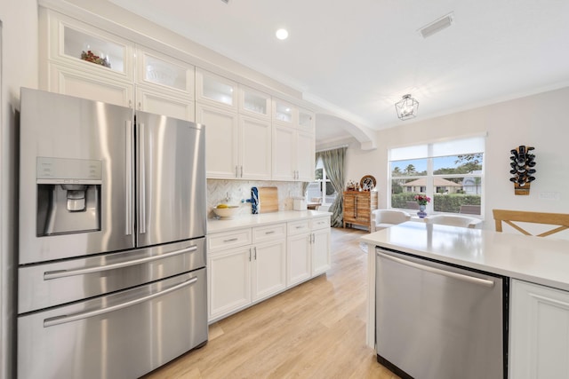 kitchen featuring white cabinetry, stainless steel appliances, light hardwood / wood-style flooring, decorative backsplash, and ornamental molding