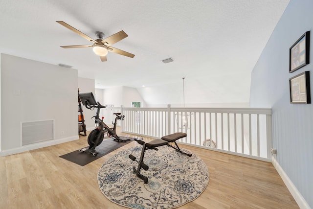 exercise room with a textured ceiling, light wood-type flooring, ceiling fan, and lofted ceiling