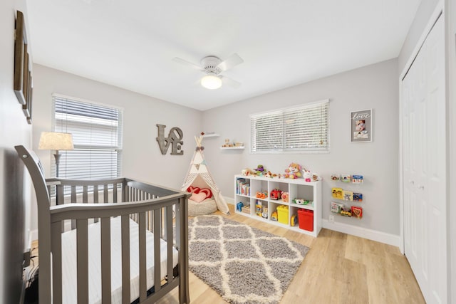 bedroom with ceiling fan, light hardwood / wood-style flooring, a nursery area, and a closet