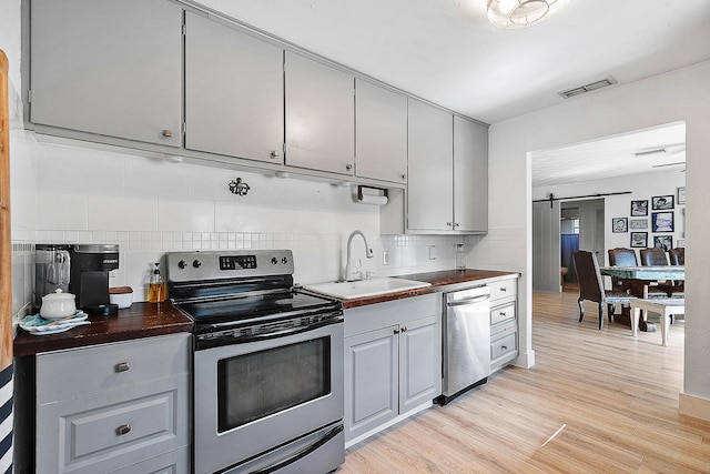 kitchen featuring sink, a barn door, backsplash, light hardwood / wood-style floors, and appliances with stainless steel finishes