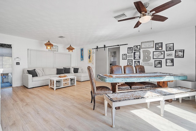 dining space with ceiling fan, a barn door, and light hardwood / wood-style floors