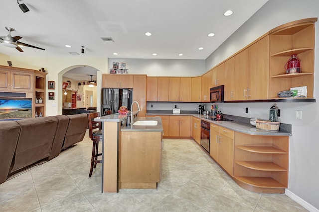 kitchen featuring light brown cabinets, a center island with sink, black appliances, sink, and ceiling fan