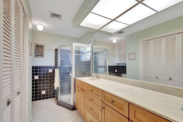 bathroom with a shower with shower door, tile walls, vanity, and tile patterned flooring