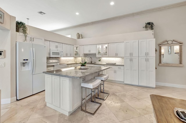 kitchen featuring sink, white cabinets, light stone counters, white appliances, and a kitchen island