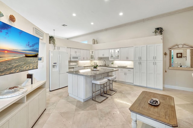 kitchen with sink, white cabinetry, white appliances, a kitchen bar, and a kitchen island