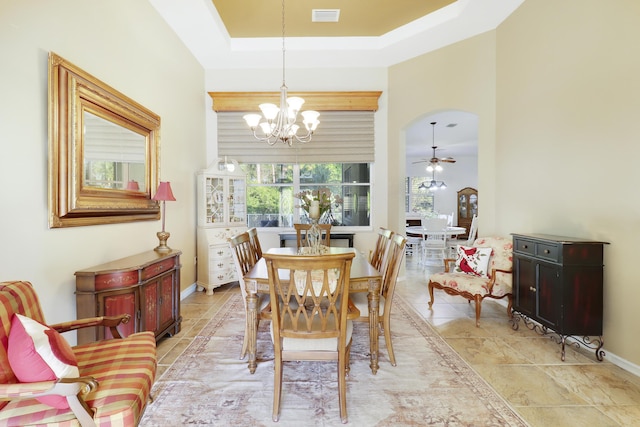 tiled dining area featuring a raised ceiling and ceiling fan with notable chandelier