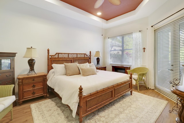 bedroom with light wood-type flooring, a raised ceiling, and ceiling fan