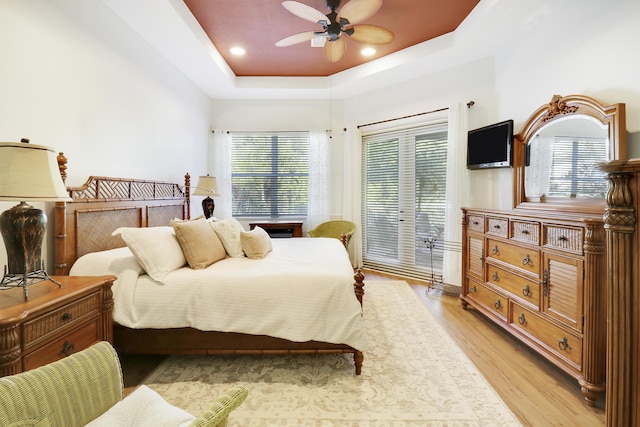 bedroom with ceiling fan, light hardwood / wood-style flooring, and a tray ceiling