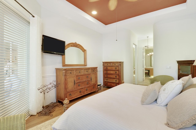 bedroom featuring multiple windows, light hardwood / wood-style floors, ceiling fan, and a tray ceiling