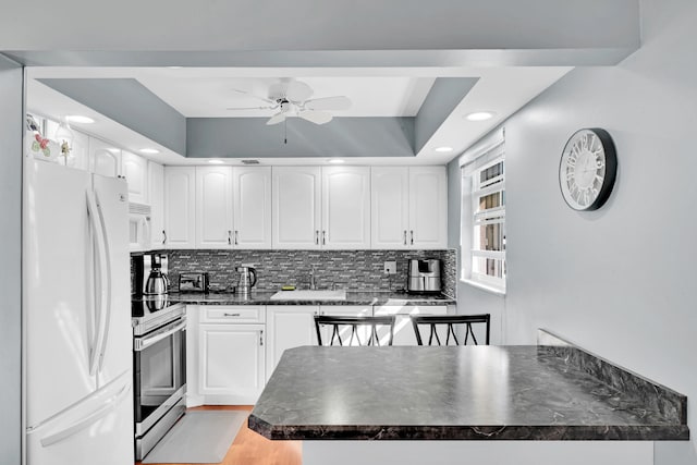 kitchen featuring a raised ceiling, white appliances, white cabinetry, and sink