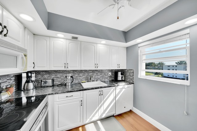 kitchen with sink, light hardwood / wood-style flooring, dark stone countertops, white cabinets, and range