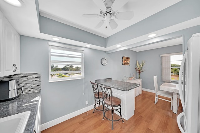 kitchen with backsplash, kitchen peninsula, light wood-type flooring, white fridge, and white cabinetry